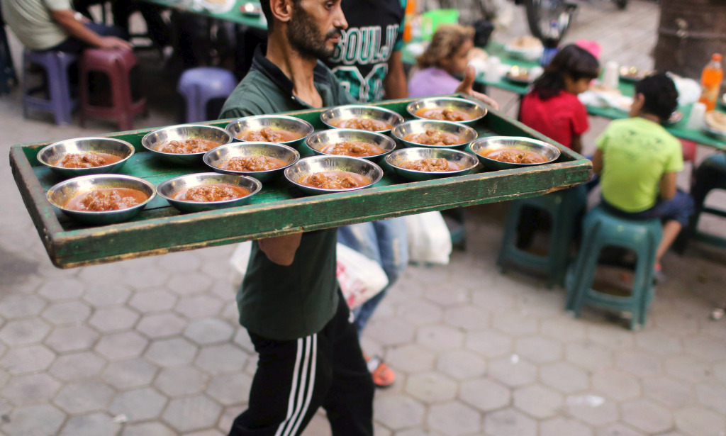 A volunteer carries food to tables as people wait to eat their Iftar meal to break their fast at charity tables that offer free food during the holy fasting month of Ramadan in Cairo, Egypt, on June 23, 2015.